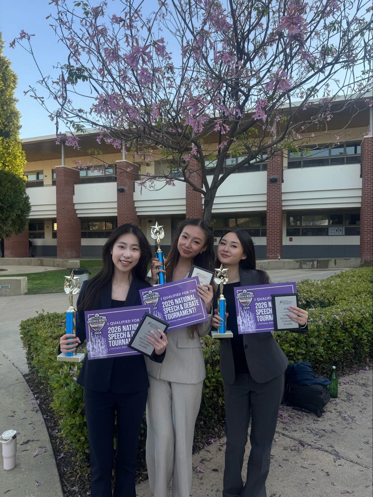 Three competitors with purple plaques under a blossoming tree