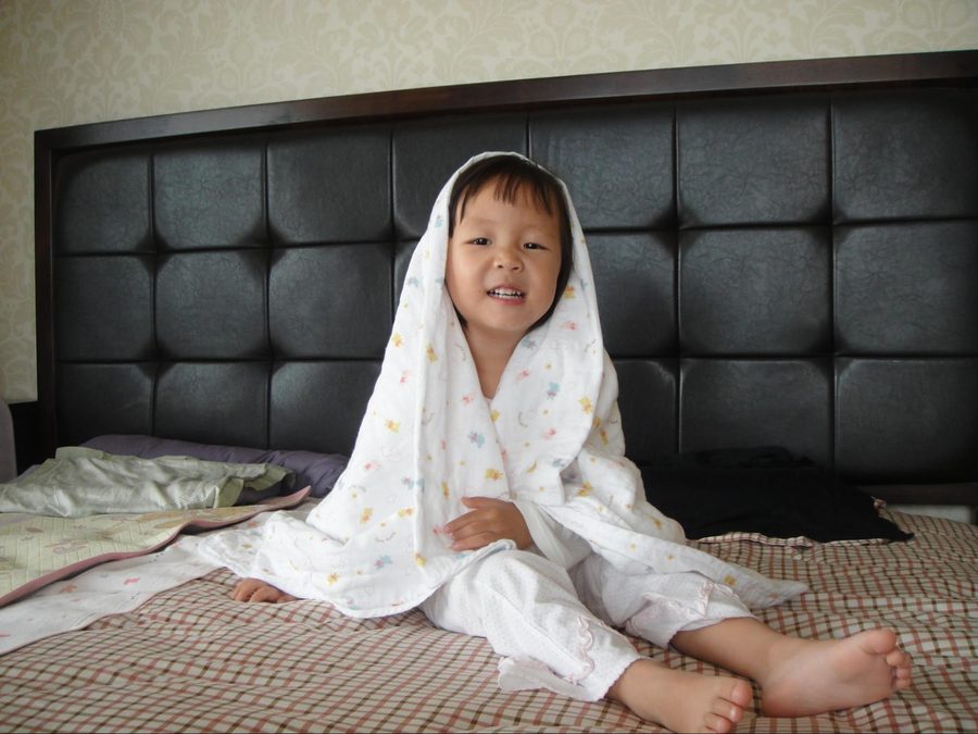 A baby sitting on a bed with a blanket over her head