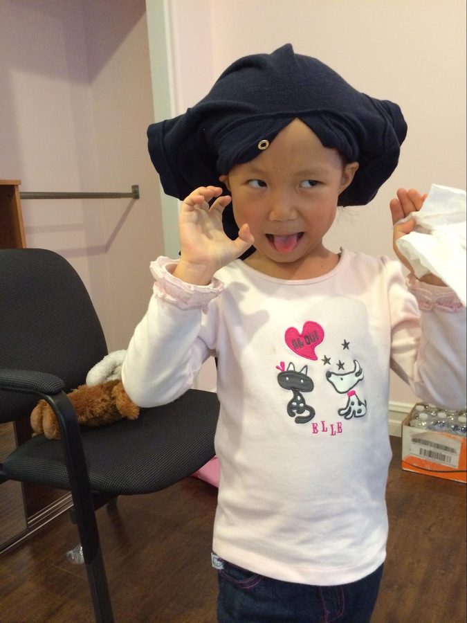 A small child pulling a knitted hat down over her ears