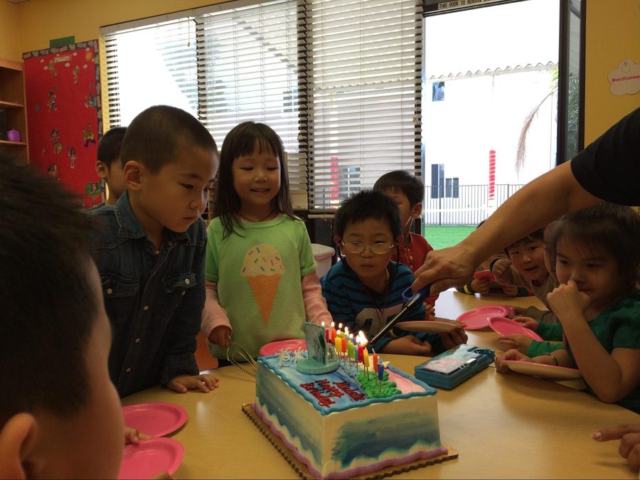 Kindergarten classmates crowded around a birthday cake with lit candles