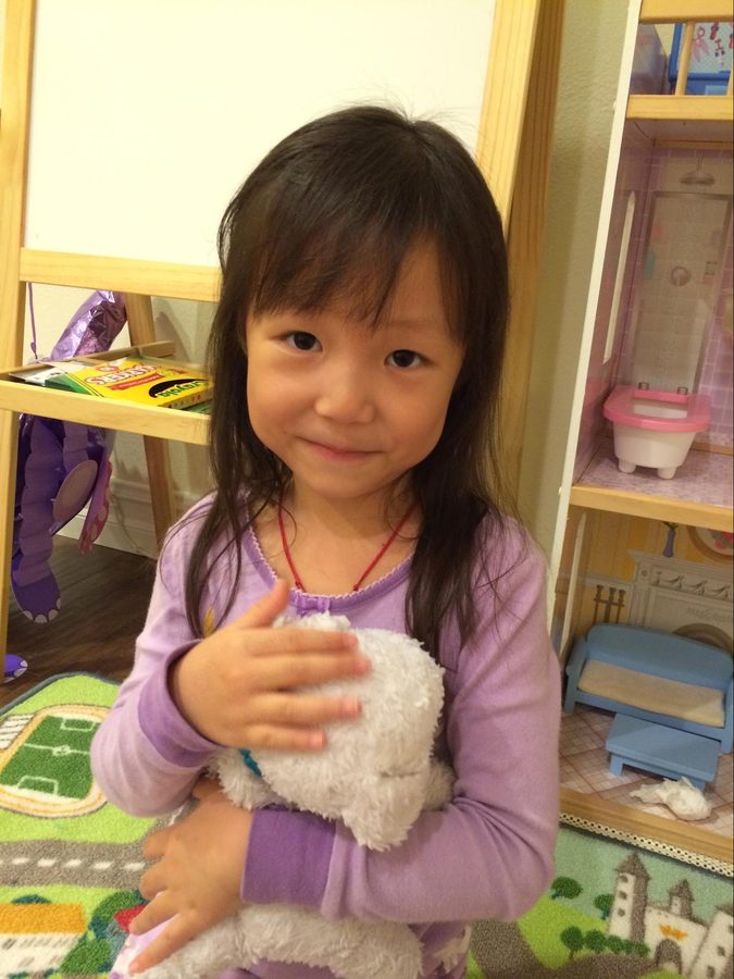 A girl holding a stuffed animal in a bedroom full of toys