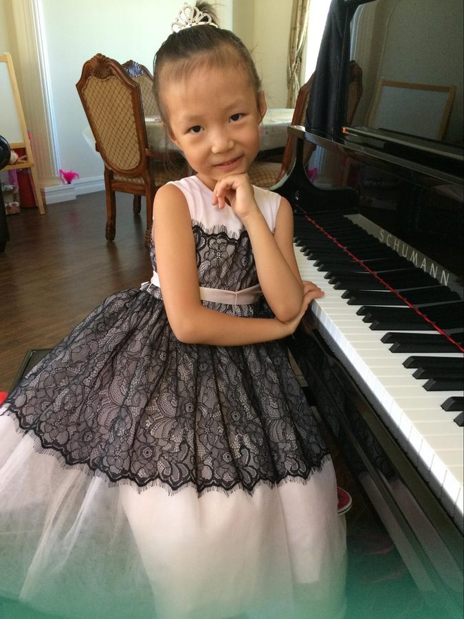 A girl in a lace recital dress posing beside a grand piano