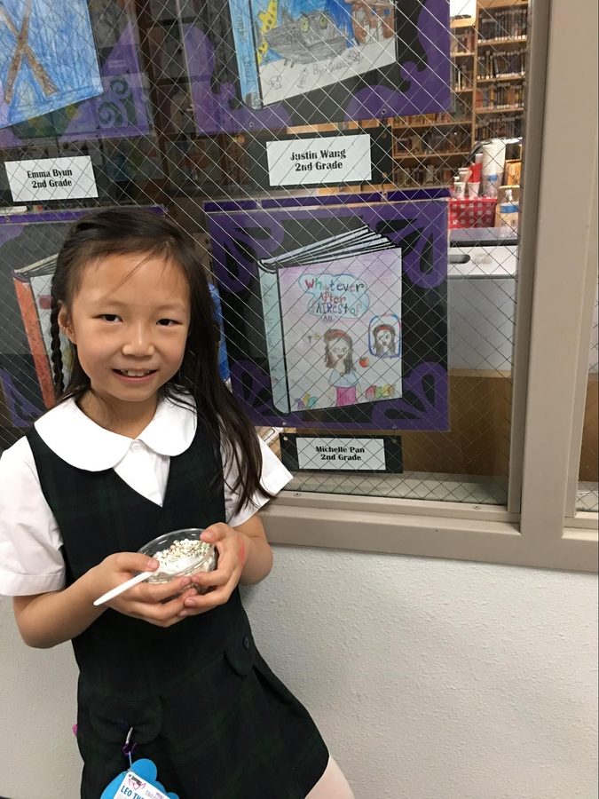A girl beaming next to her artwork pinned up on a school wall