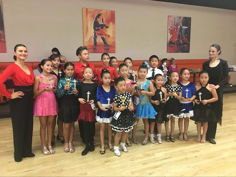 A whole ballroom class lined up on stage holding trophies