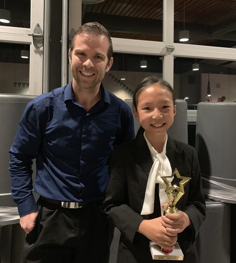 Michelle in a blazer holding a star trophy beside her coach